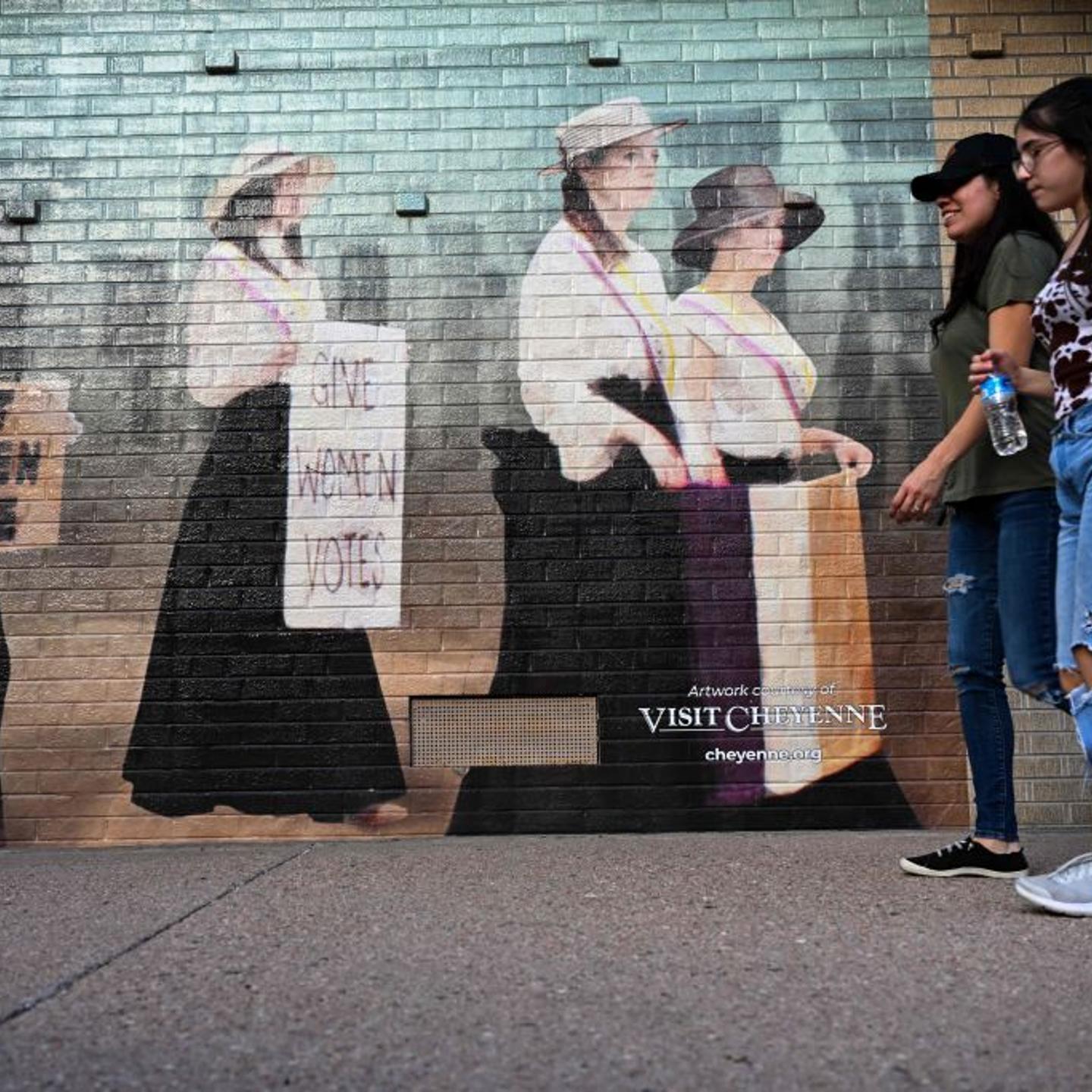People walk past a mural of featuring a representation of women seeking the right to vote,
