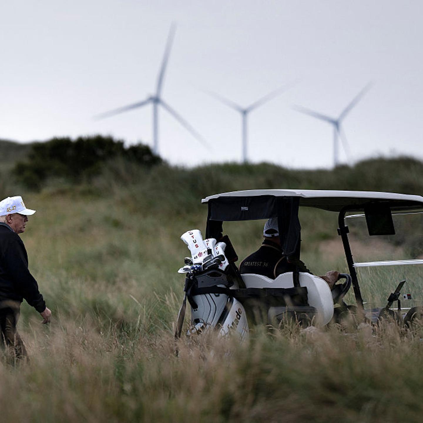 Trump walking on a golf course with wind turbines offshore in the background