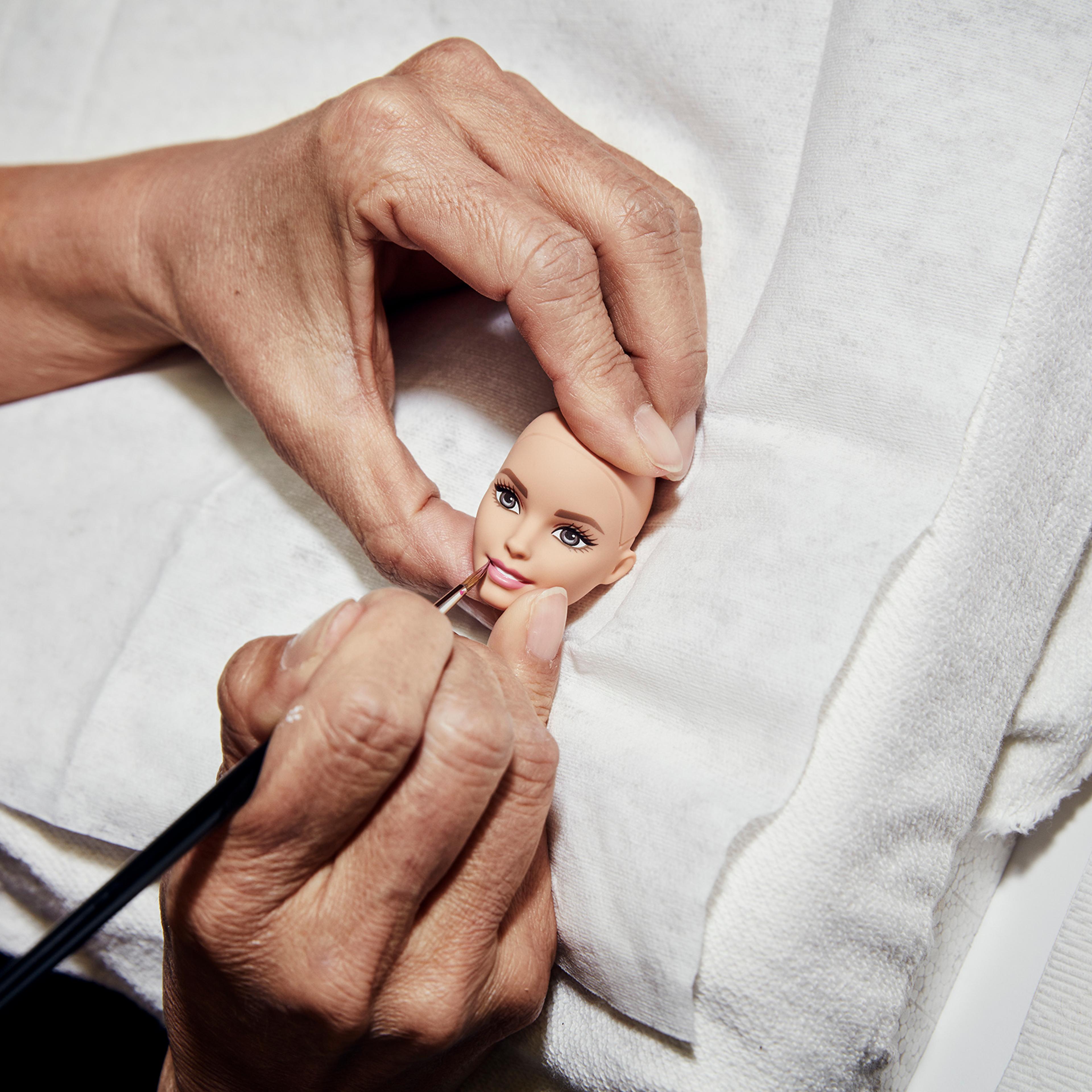 A designer hand paints the lips of a prototype Barbie doll.
