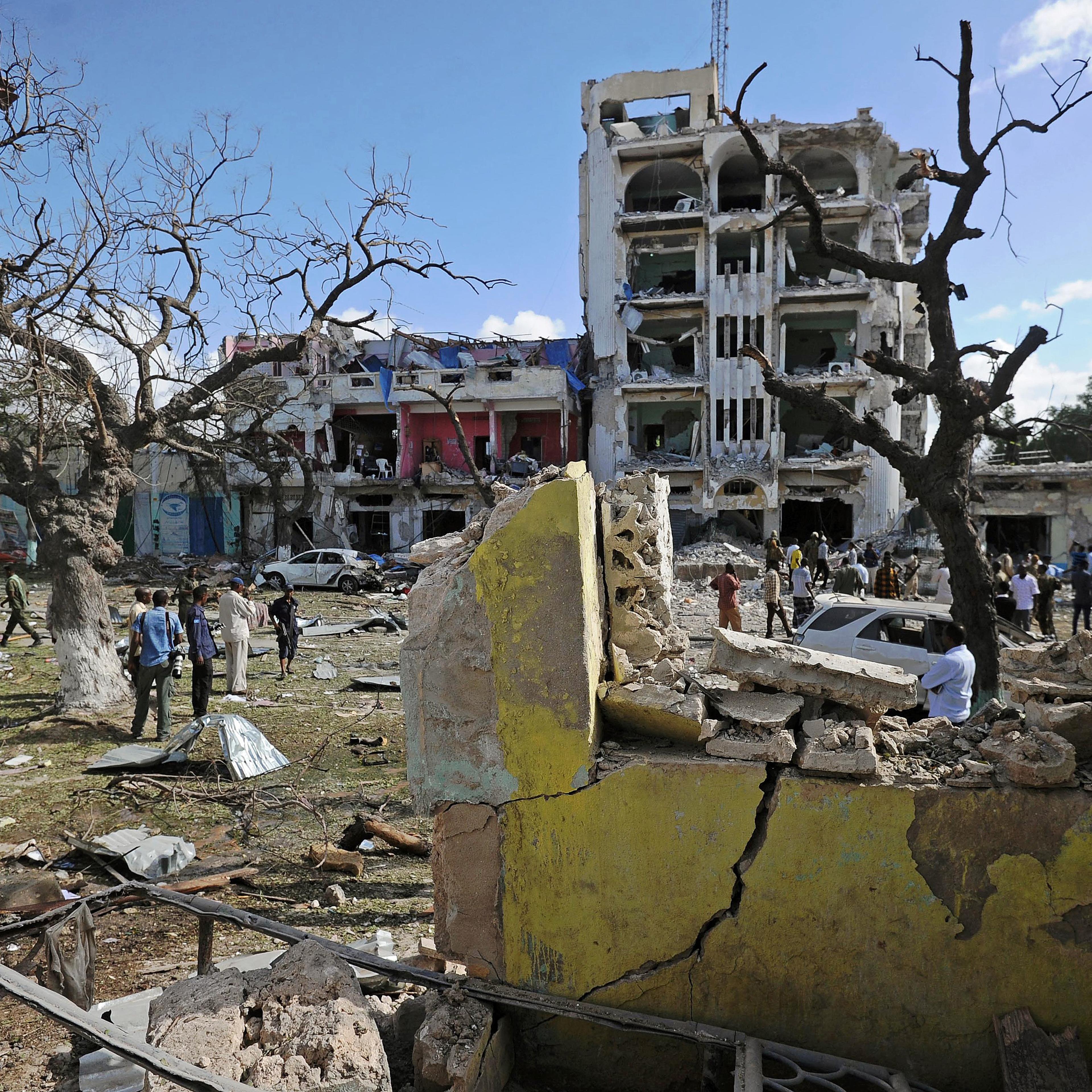People stand on the scene of a terror attack outside The Ambassador Hotel in Mogadishu on June 2, 2016.