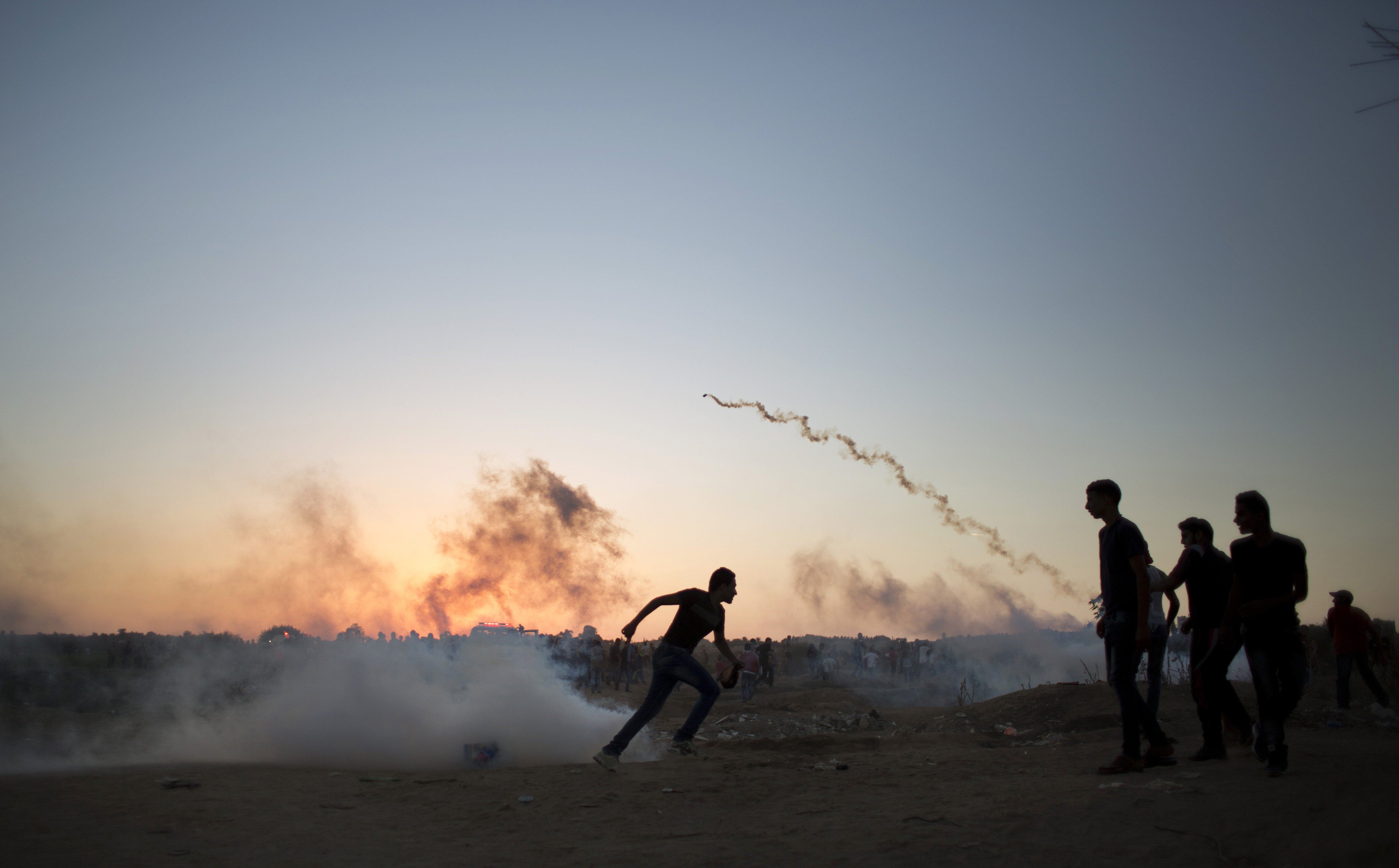 Palestinian protesters run for cover from tear gas fired by Israeli soldiers during clashes on the Israeli border with Gaza in Buriej, central Gaza Strip on Oct. 15, 2015.