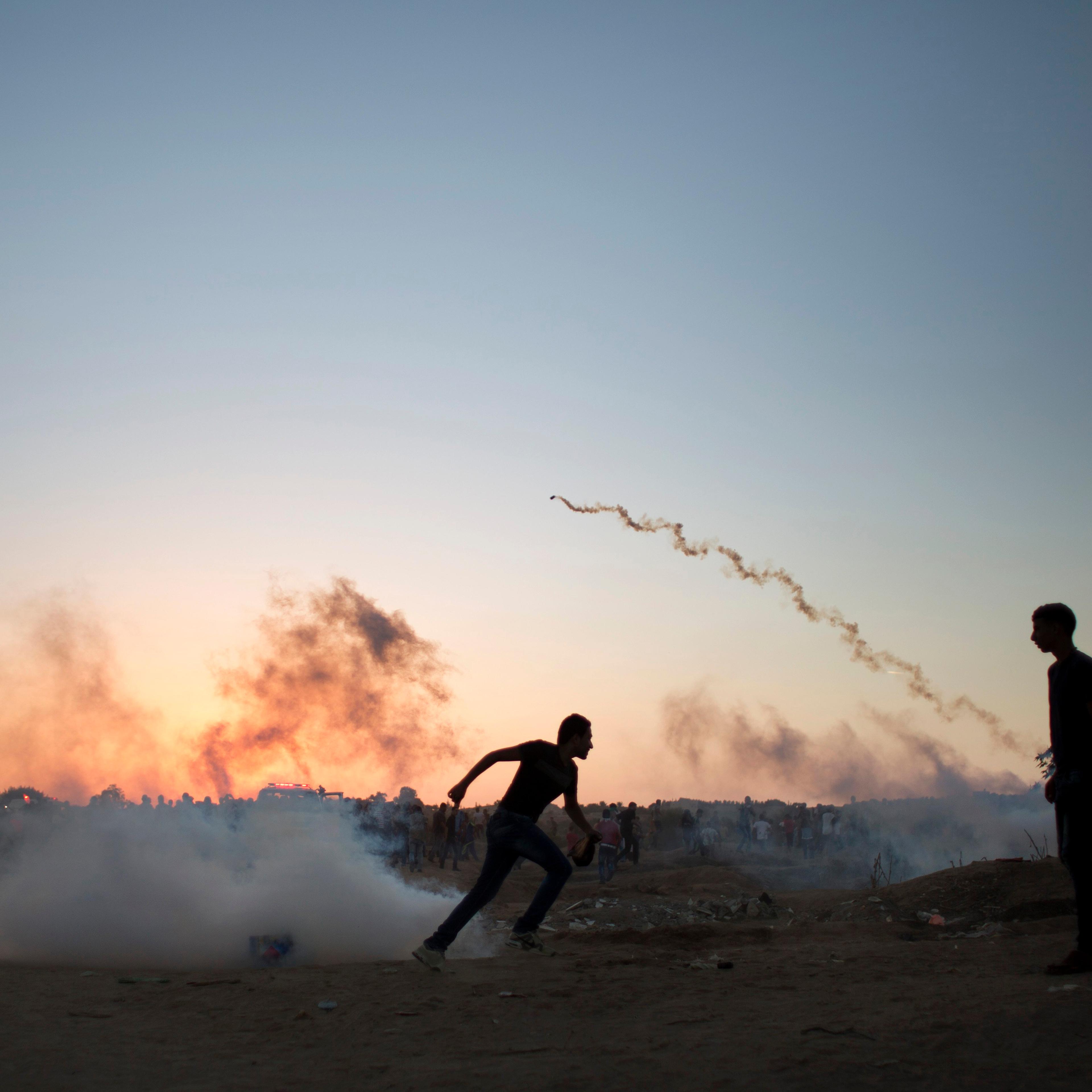 Palestinian protesters run for cover from tear gas fired by Israeli soldiers during clashes on the Israeli border with Gaza in Buriej, central Gaza Strip on Oct. 15, 2015.