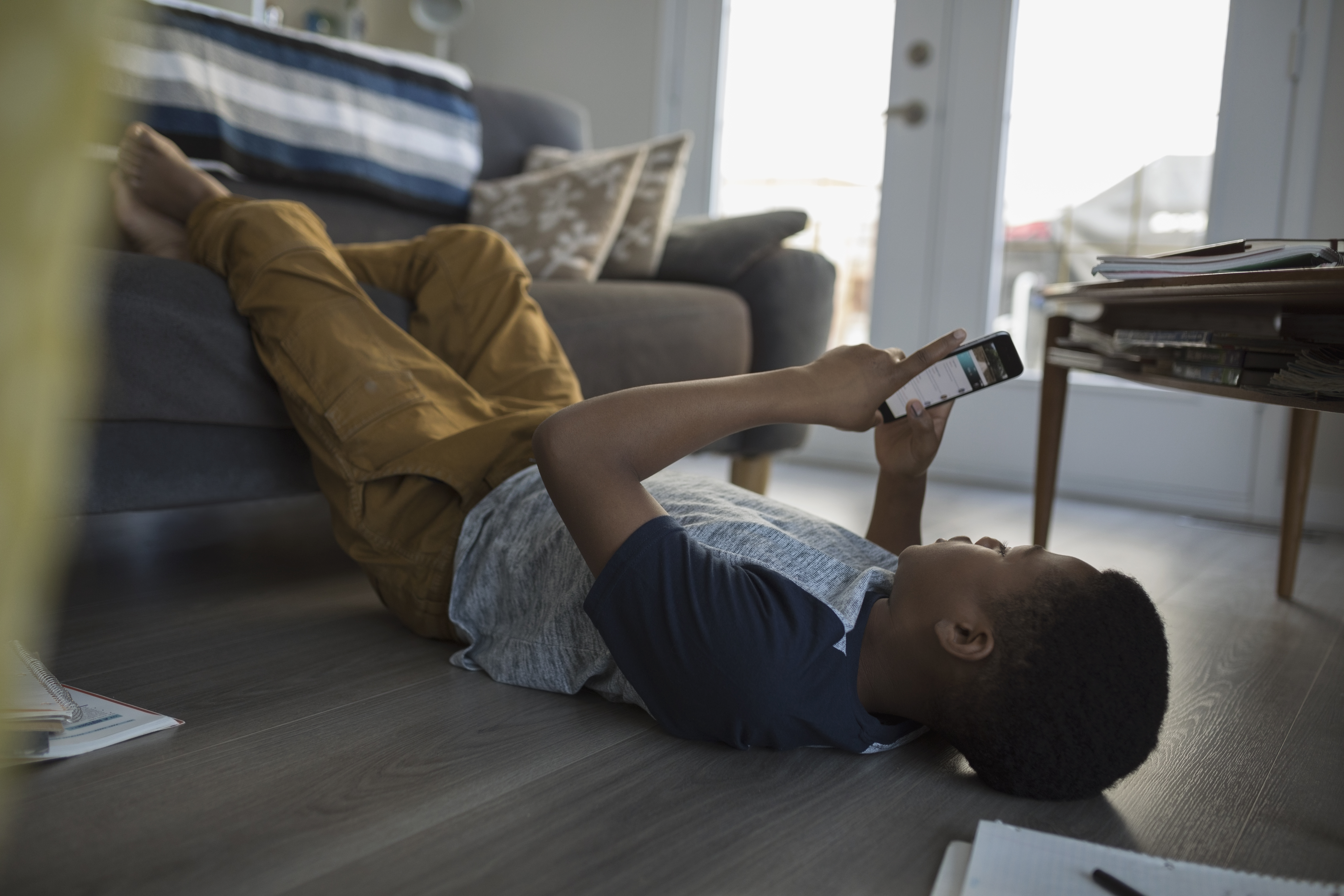 Teenage boy laying, using cell phone on living room sofa