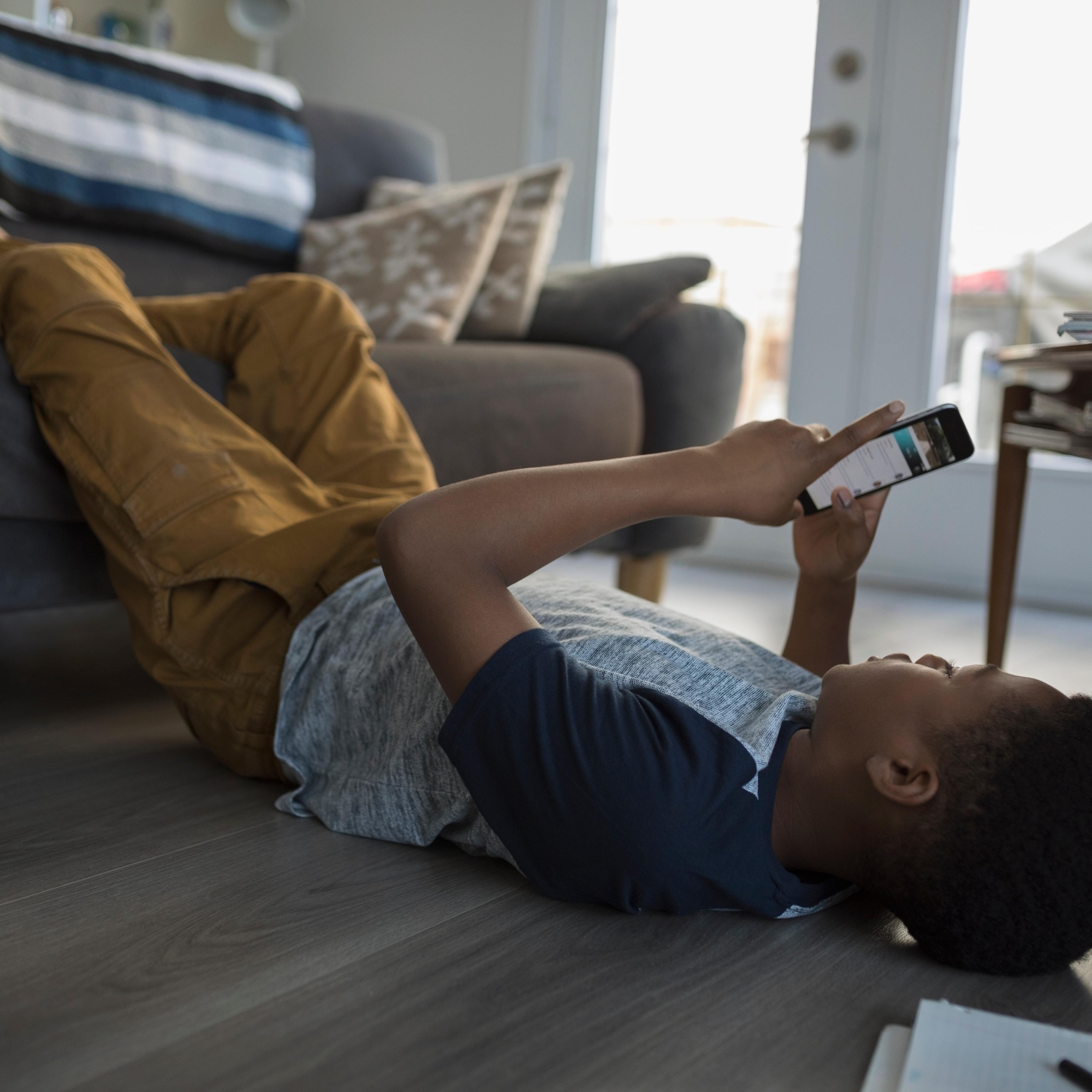 Teenage boy laying, using cell phone on living room sofa