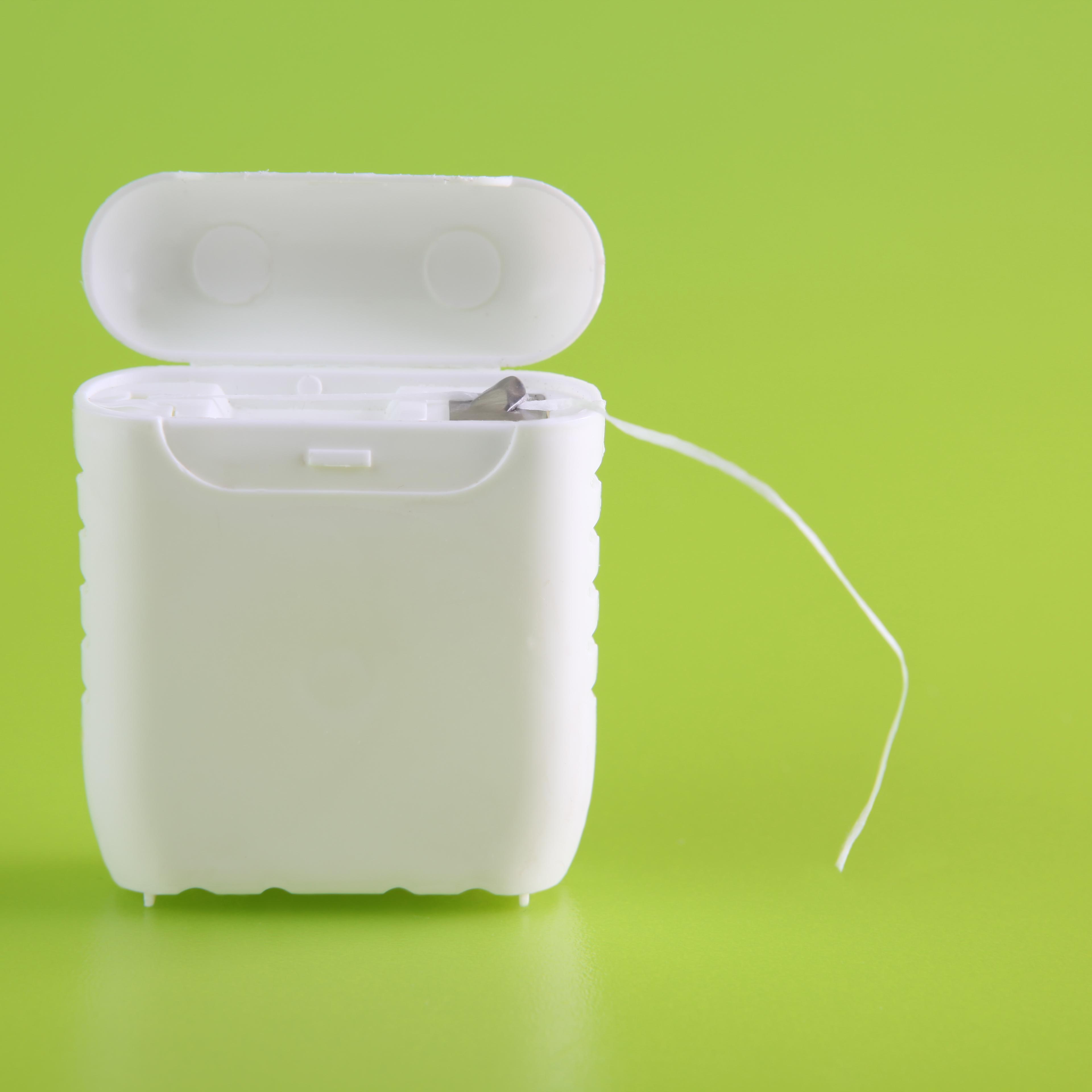 A close-up of a dental floss container on bright green