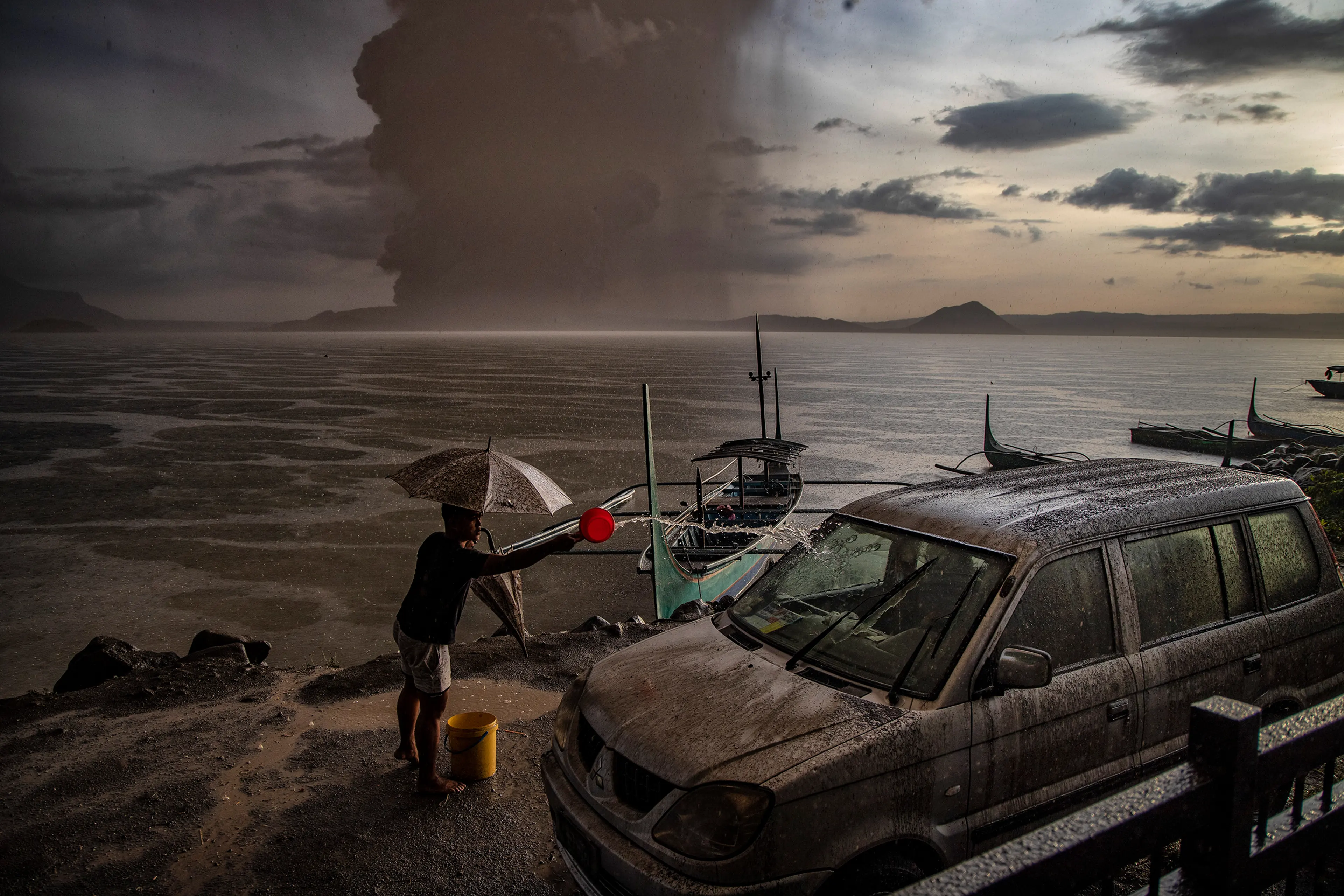 A resident in Talisay splashes water on a vehicle covered in ash mixed with rainwater as the Taal volcano erupts on Jan. 12.