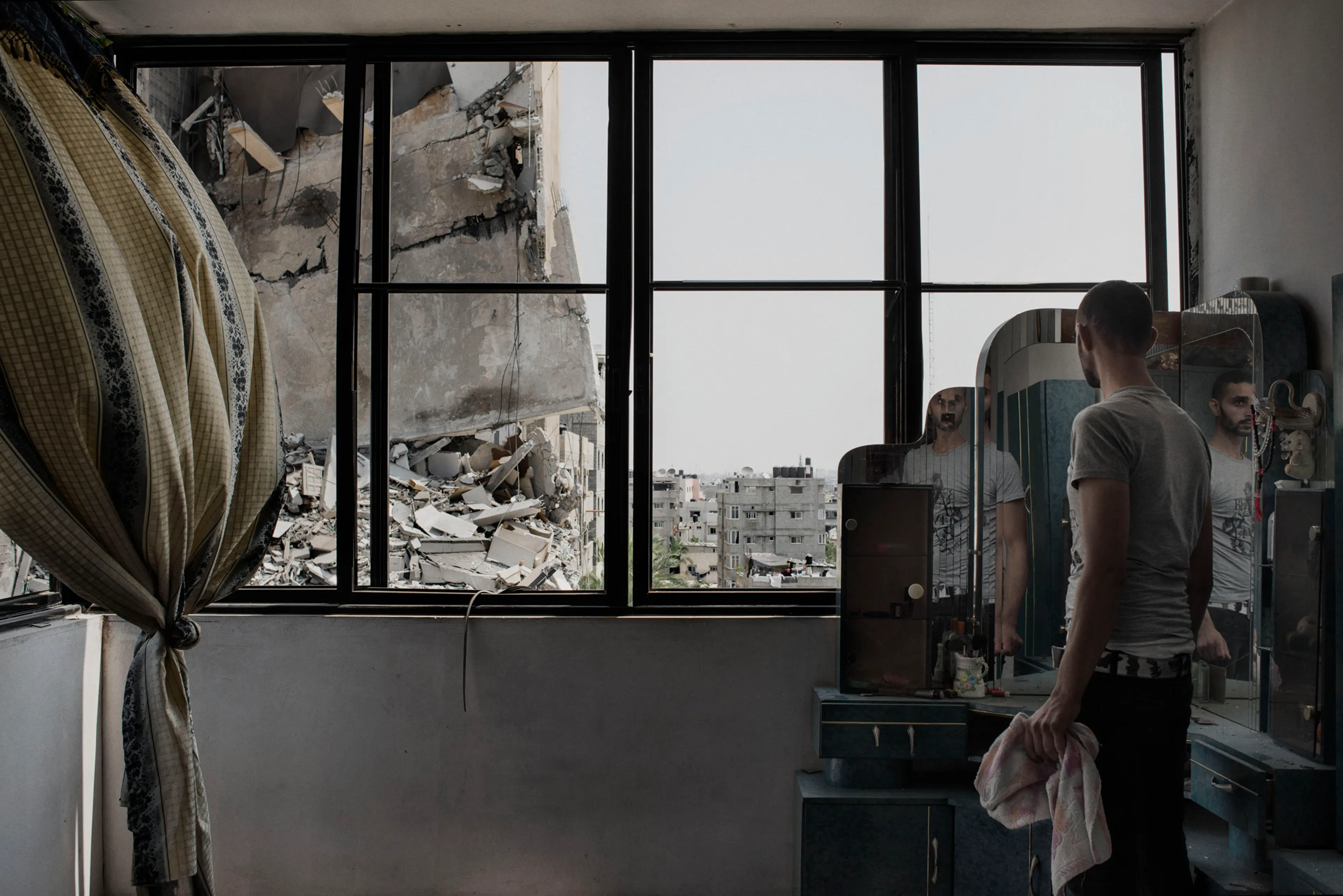 Gaza Strip, Gaza Street: A Palestinian man looks through the window of his house at the buildings damaged overnight by an airstrike in Gaza City.. ALESSIO ROMENZI for TIME