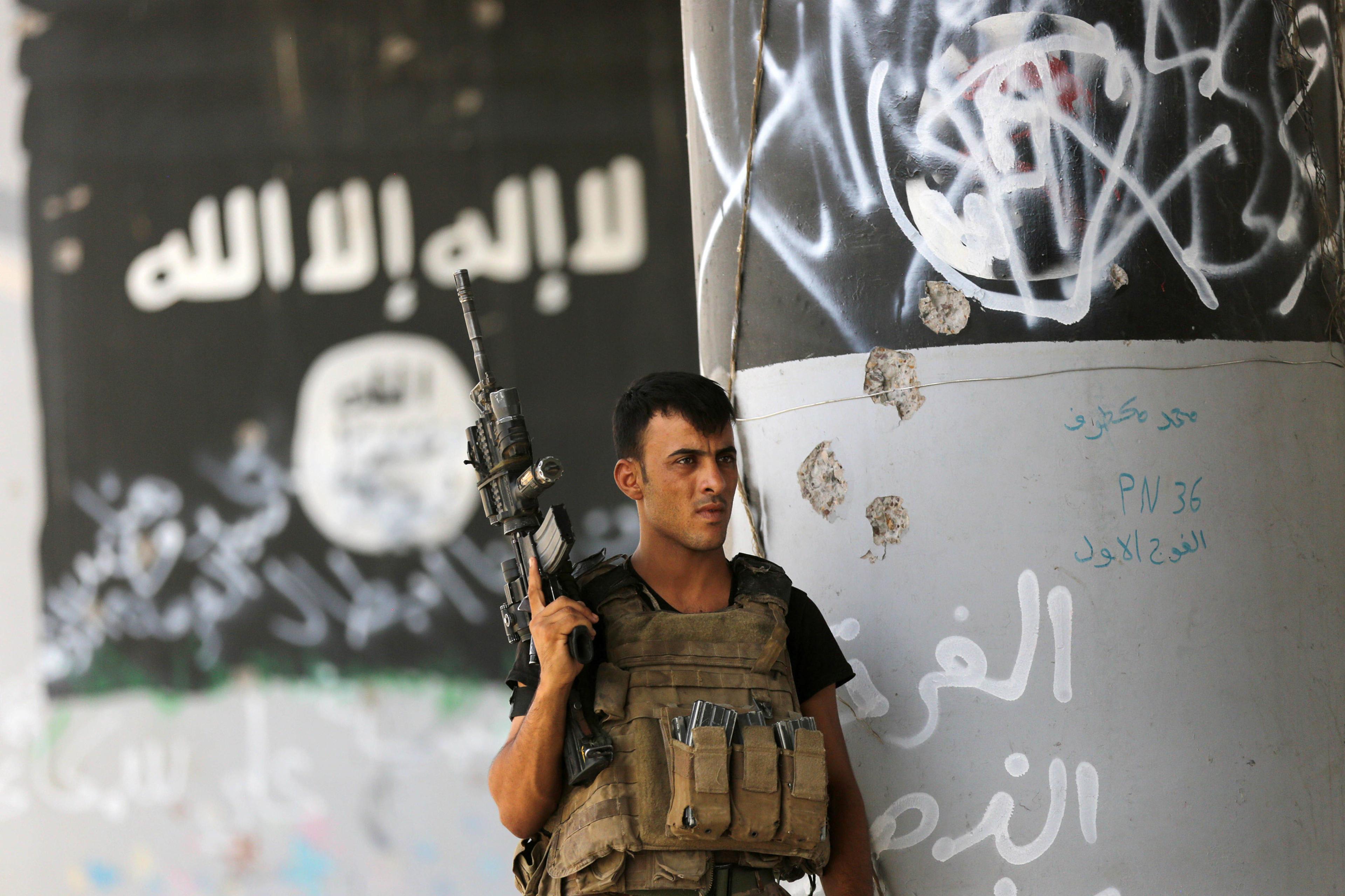 A member of Iraqi counterterrorism forces stands guard near Islamic State militant graffiti in Fallujah, Iraq, Monday, June 27, 2016. Thick clouds of black smoke billowed over northwest Fallujah Monday as dozens of homes continued to burn a day after the