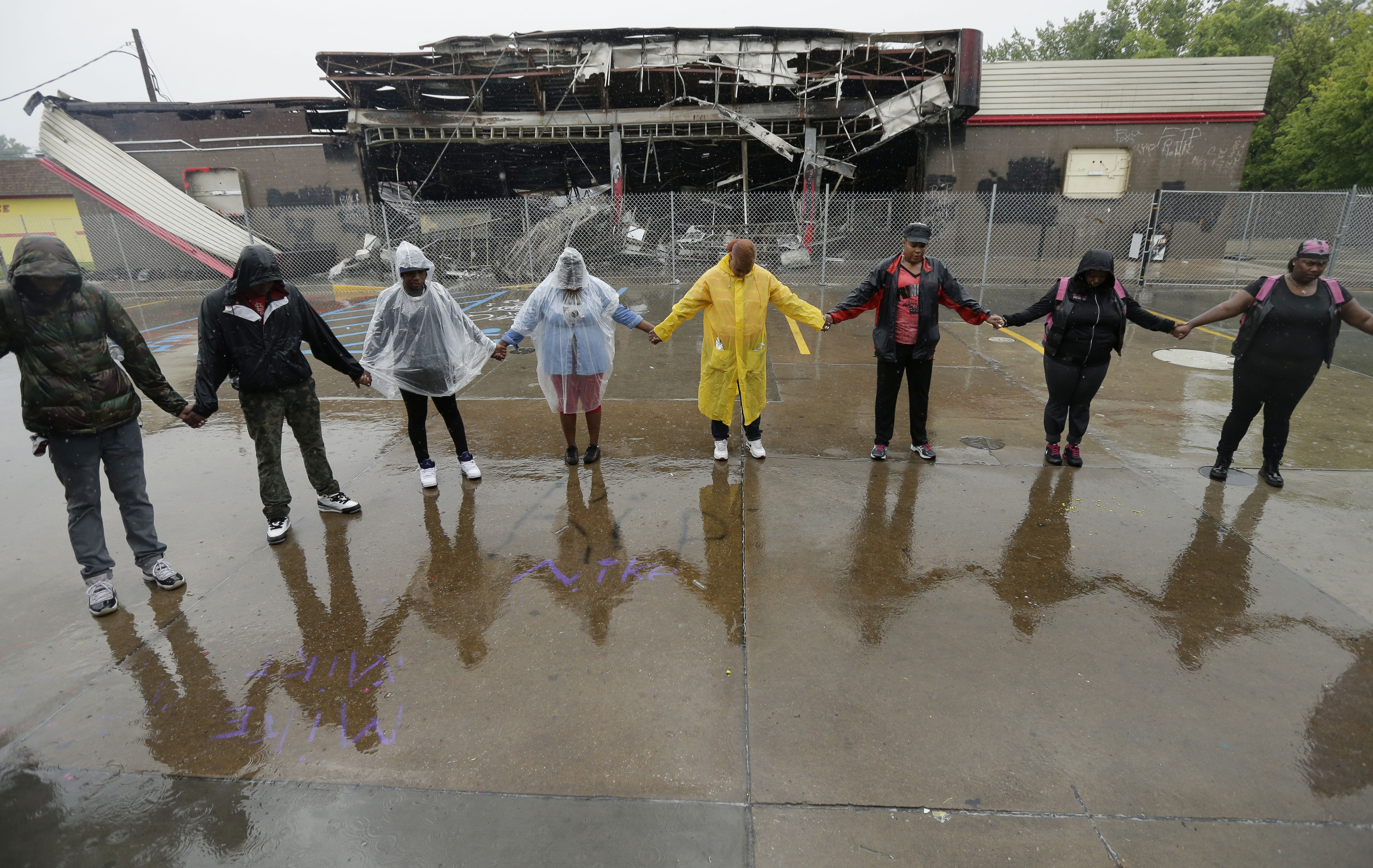 People hold hands in prayer on Aug. 16, 2014, at a convenience store that was burned after Michael Brown was shot by police a week ago in Ferguson, Mo.
