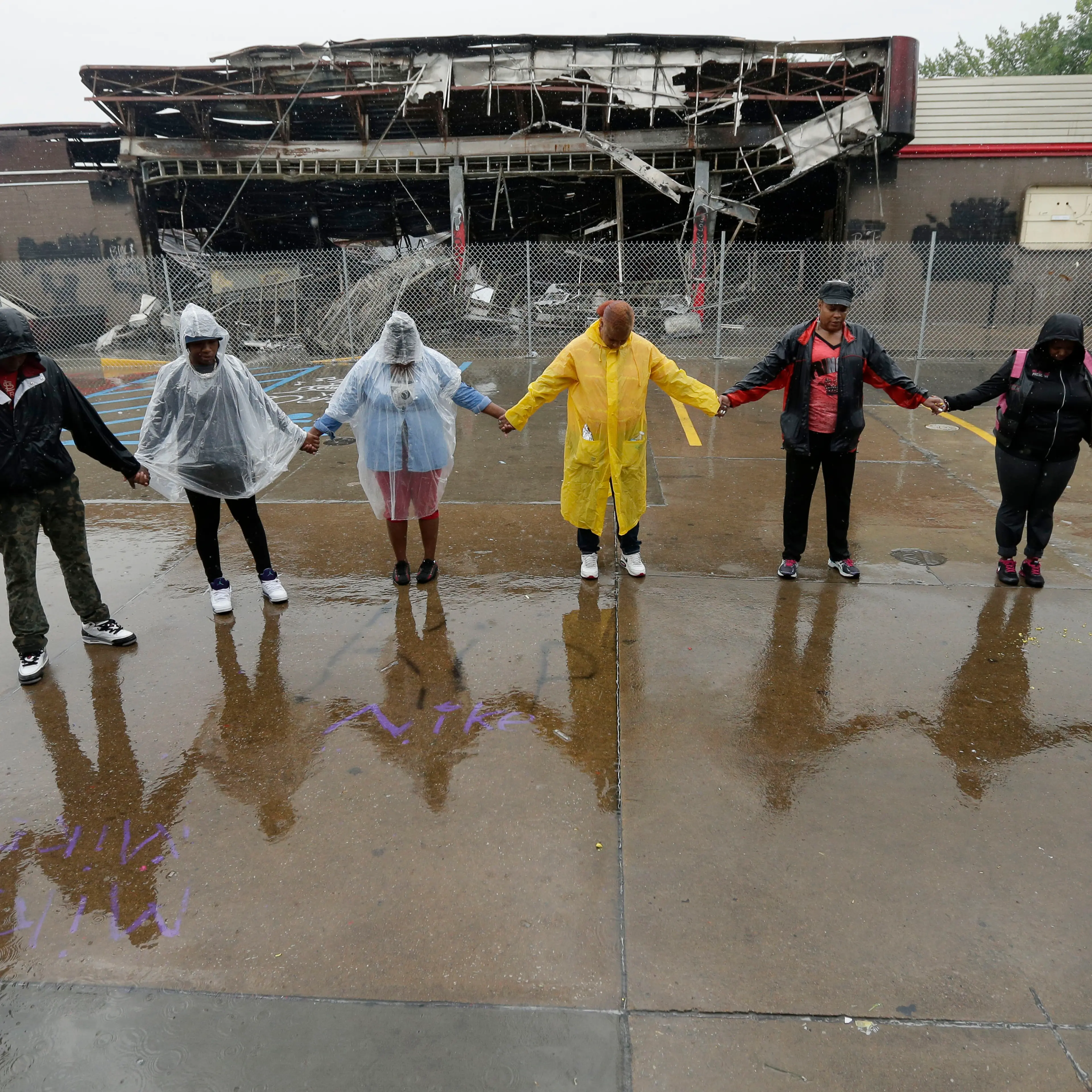 People hold hands in prayer on Aug. 16, 2014, at a convenience store that was burned after Michael Brown was shot by police a week ago in Ferguson, Mo.