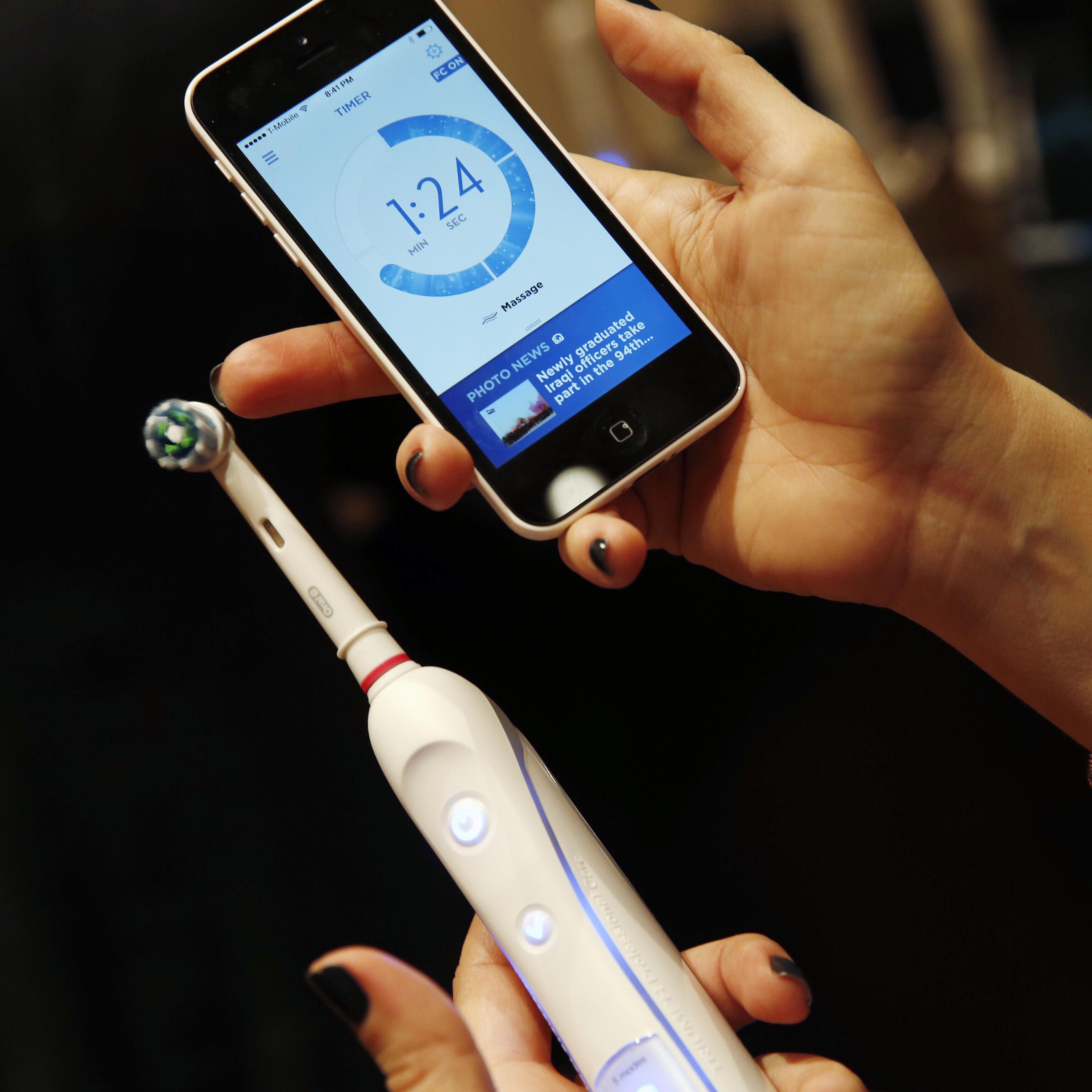 An attendee holds an Procter & Gamble Co. Oral-B SmartSeries electric toothbrush alongside an Apple Inc. iPhone during the 2015 Consumer Electronics Show (CES) in Las Vegas, Nevada, U.S., on Tuesday, Jan. 6, 2015.