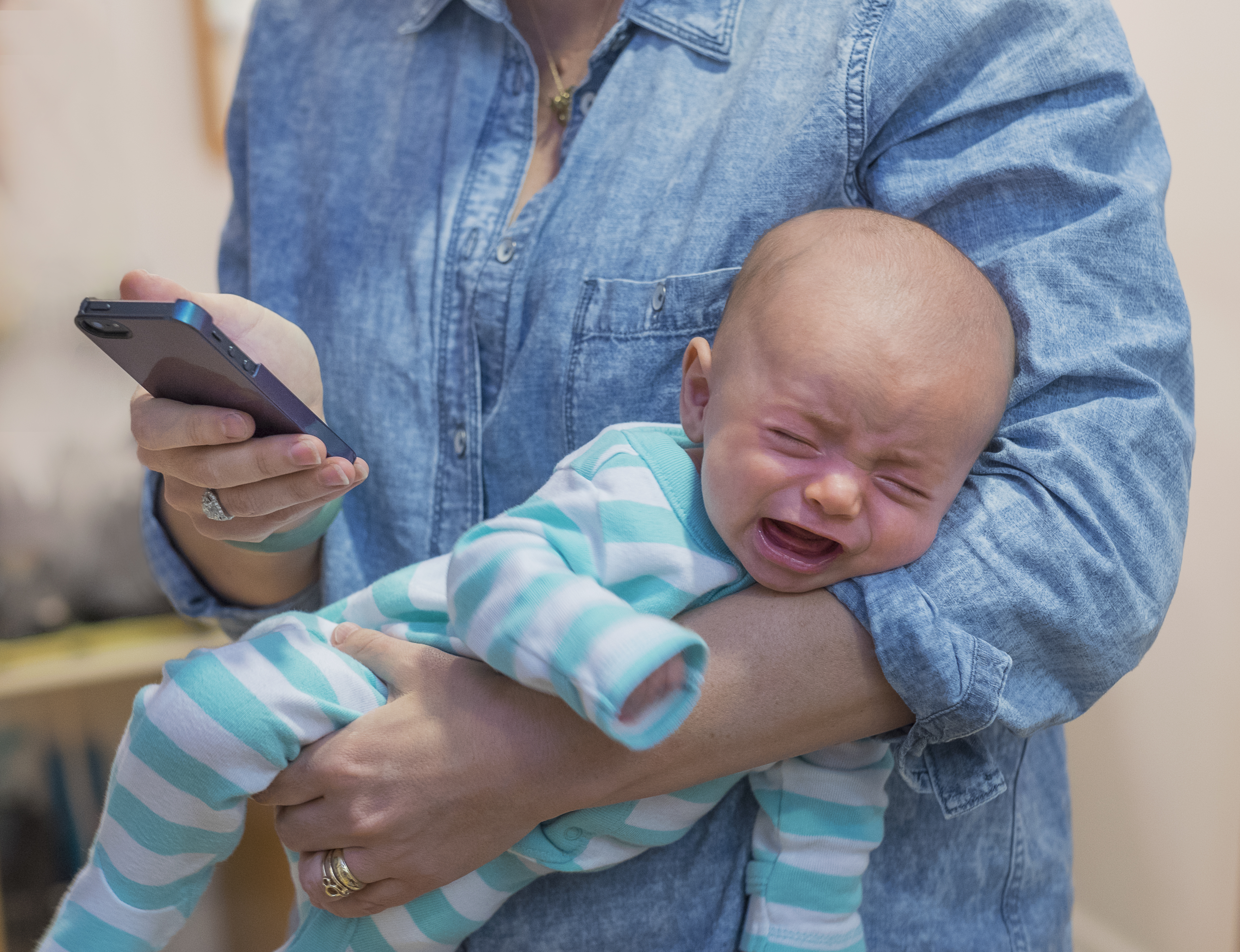 USA, New Jersey, Jersey City, Woman texting and holding crying baby boy (2-5 months)