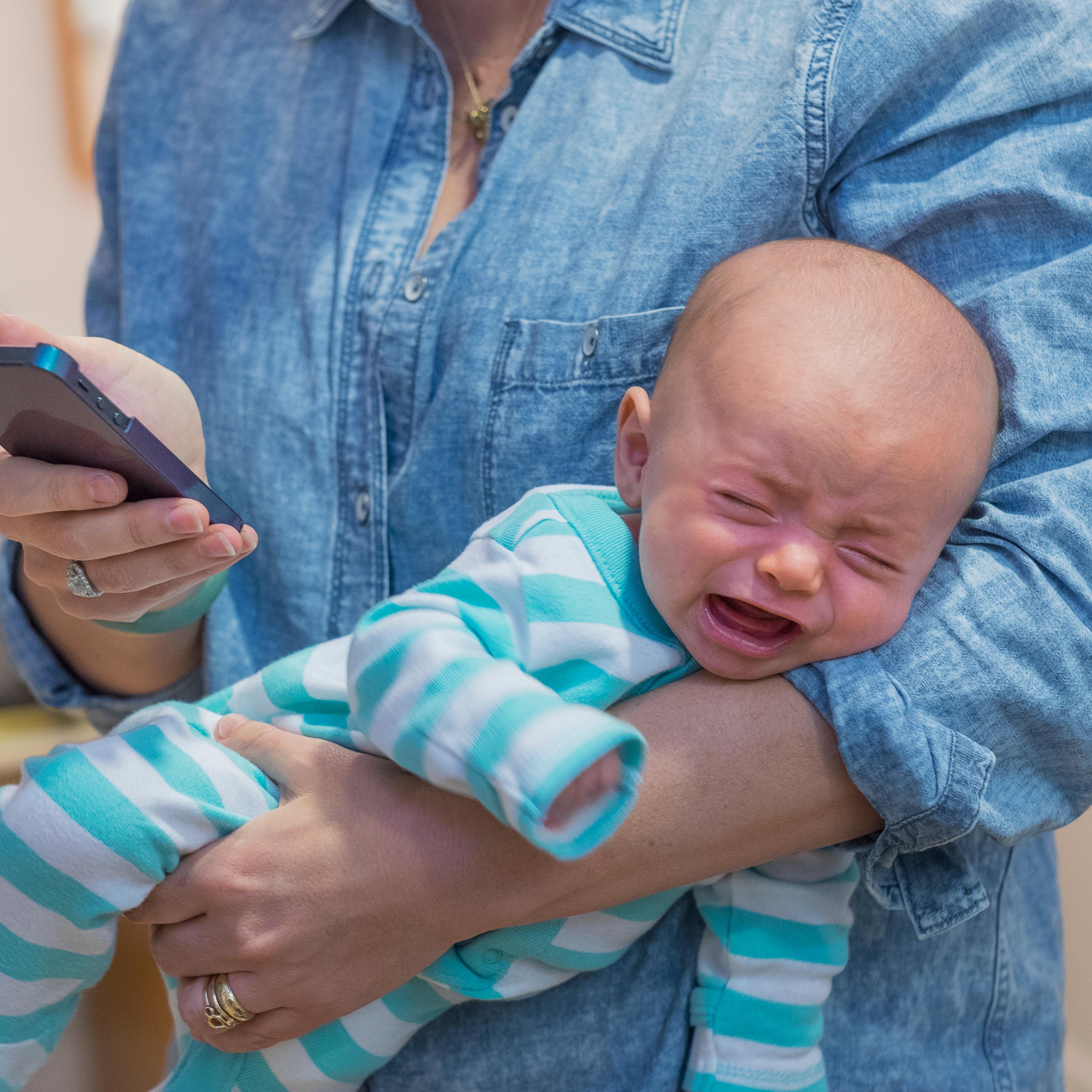 USA, New Jersey, Jersey City, Woman texting and holding crying baby boy (2-5 months)