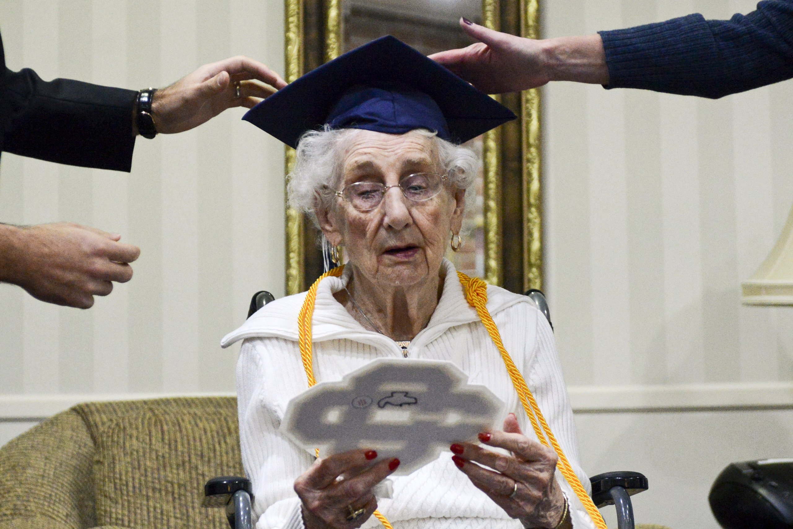 97-year-old Margaret Thome Bekema looks at her high school letter as Catholic Central High School principal Greg Deja, left, and Director of Advancement Beth Banta fix her cap shortly after her honorary graduation at Stonebridge Manor on Thursday, Oct. 2