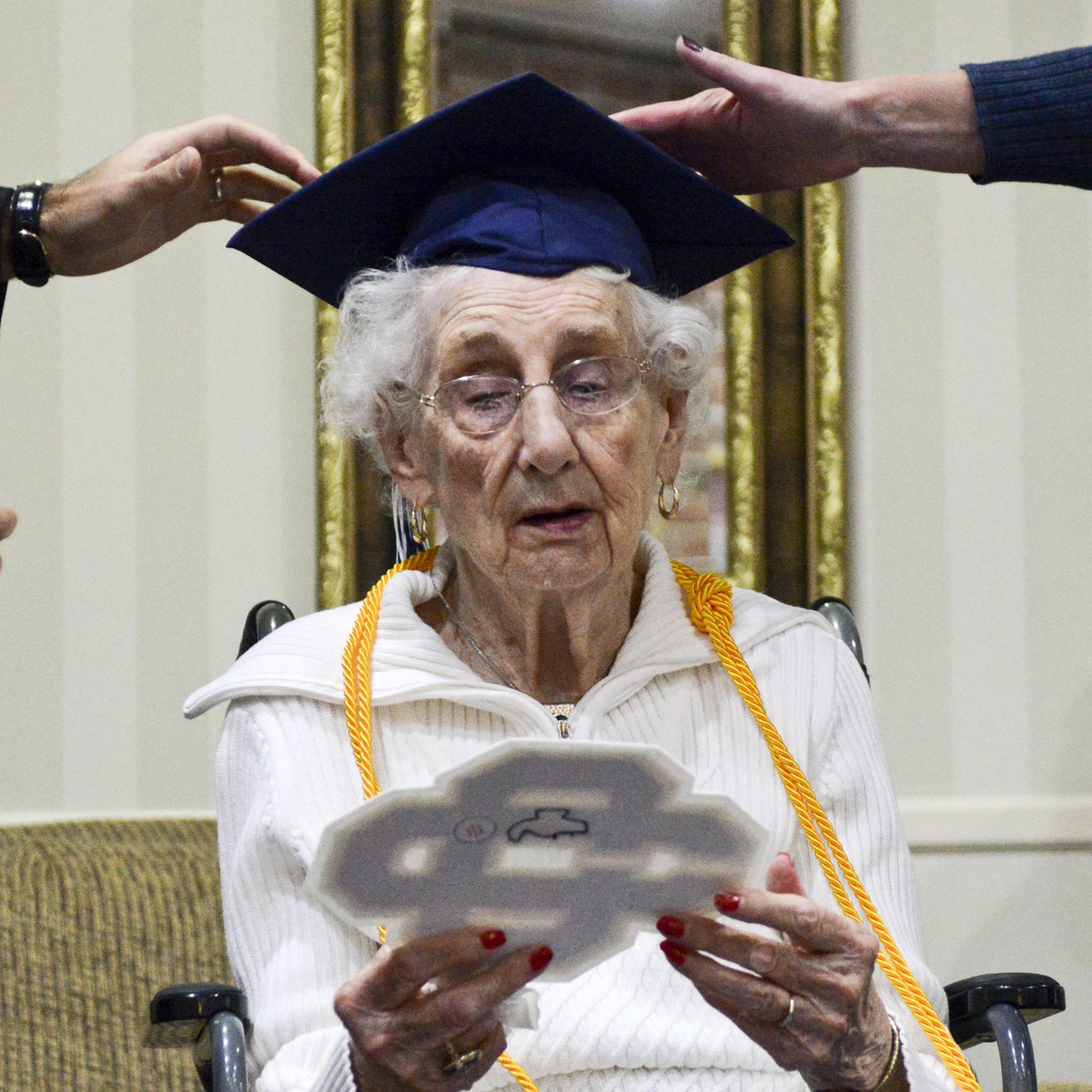 97-year-old Margaret Thome Bekema looks at her high school letter as Catholic Central High School principal Greg Deja, left, and Director of Advancement Beth Banta fix her cap shortly after her honorary graduation at Stonebridge Manor on Thursday, Oct. 2