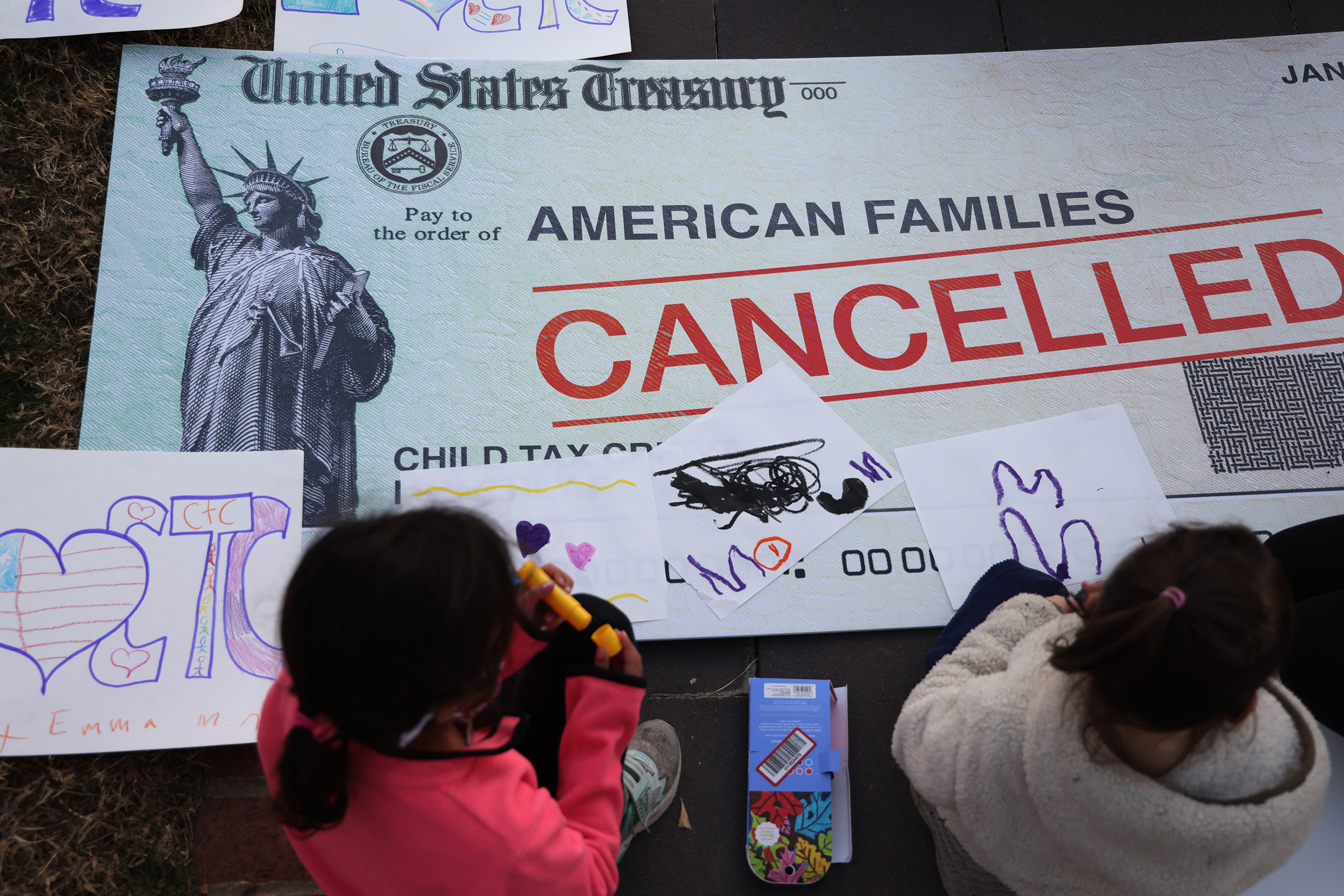 Children draw on top of a 'cancelled check' prop during a rally urging the passage of the Build Back Better legislation to extend the expanded Child Tax Credit, in front of the U.S. Capitol in Washington, D.C., on Dec. 13, 2021.