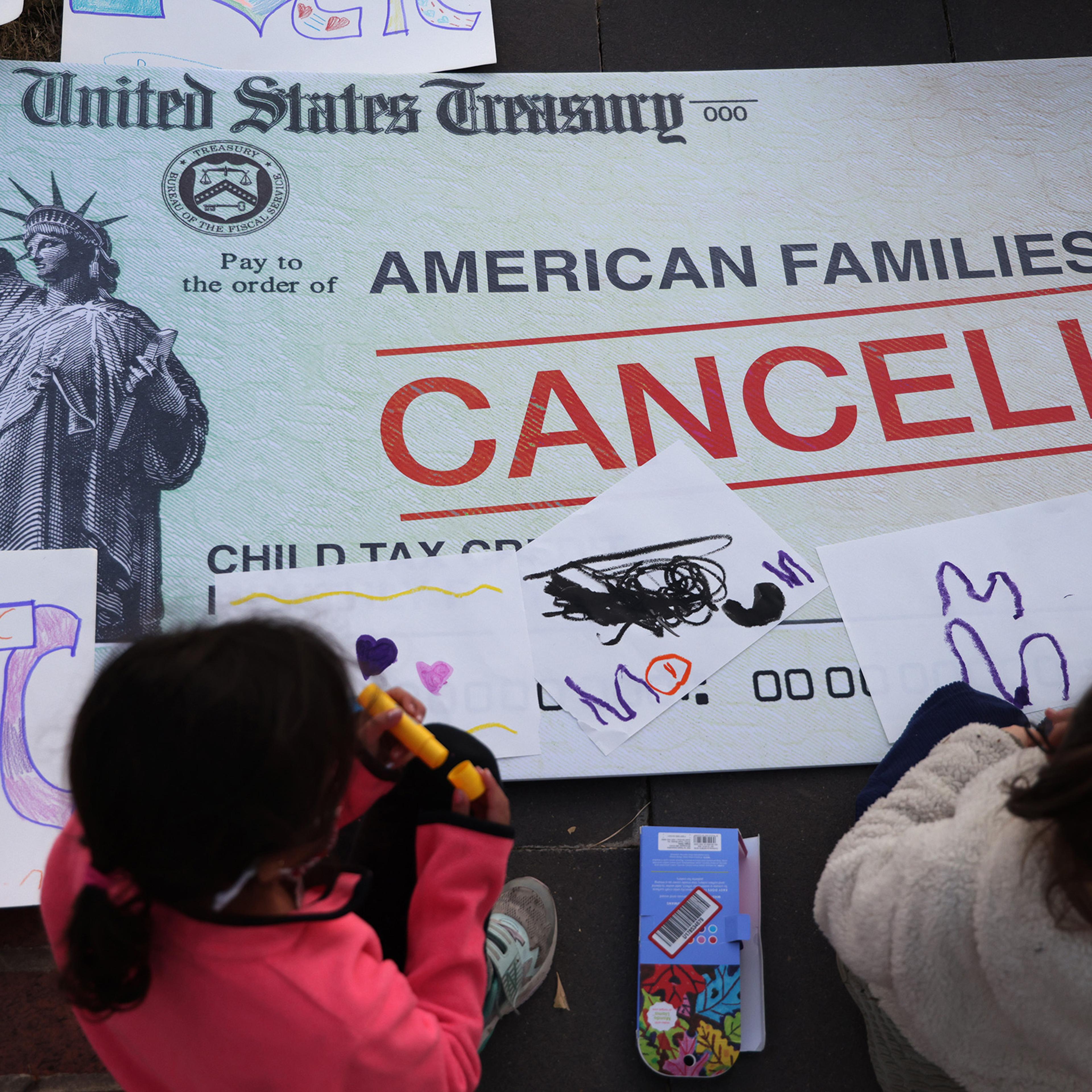 Children draw on top of a 'cancelled check' prop during a rally urging the passage of the Build Back Better legislation to extend the expanded Child Tax Credit, in front of the U.S. Capitol in Washington, D.C., on Dec. 13, 2021.