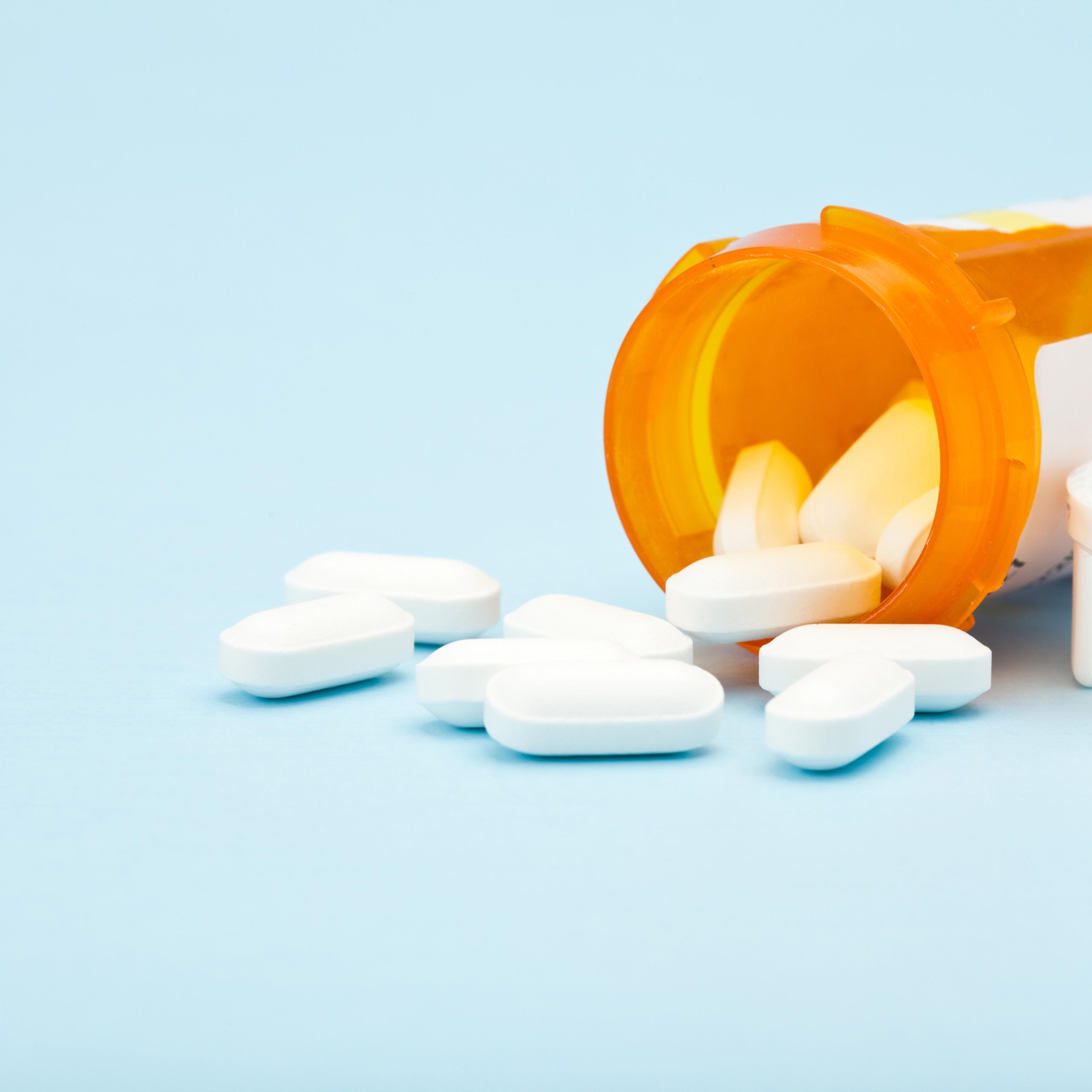Pills spilling out from medicine bottle on blue background