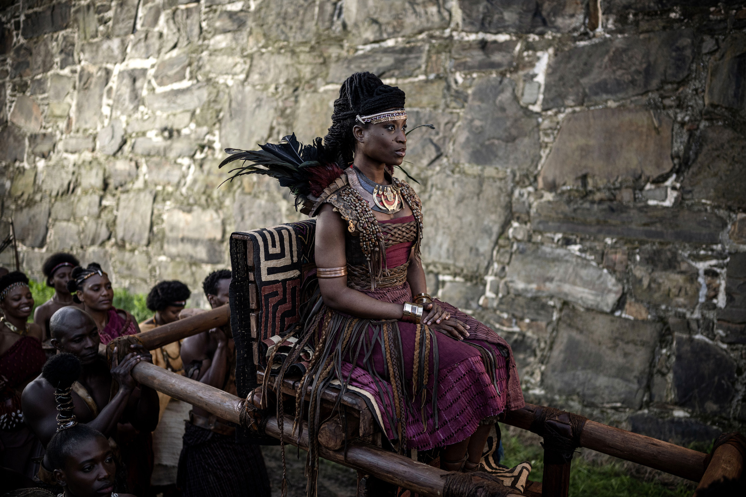 Njinga sits on a litter carried by men walking underneath her.