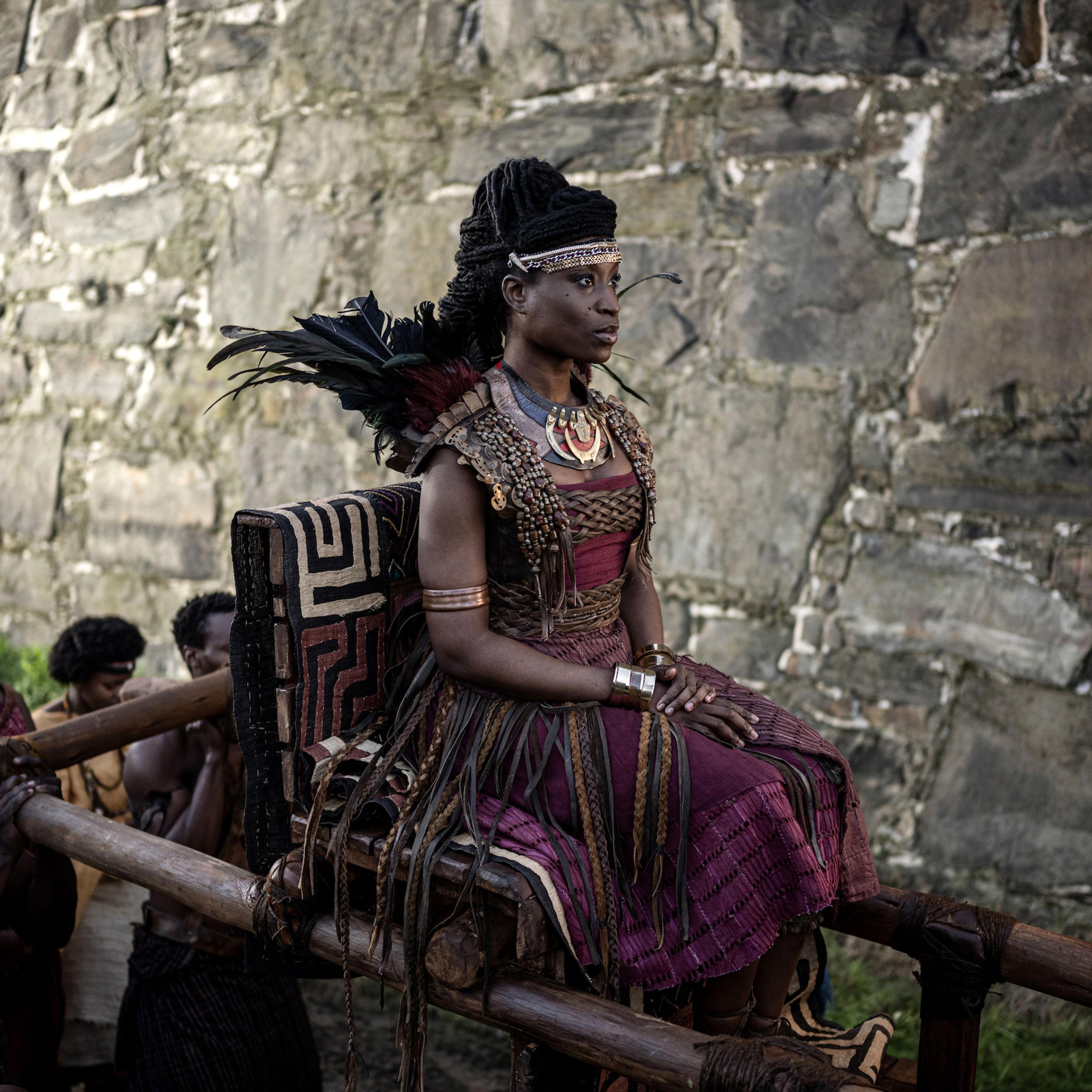 Njinga sits on a litter carried by men walking underneath her.