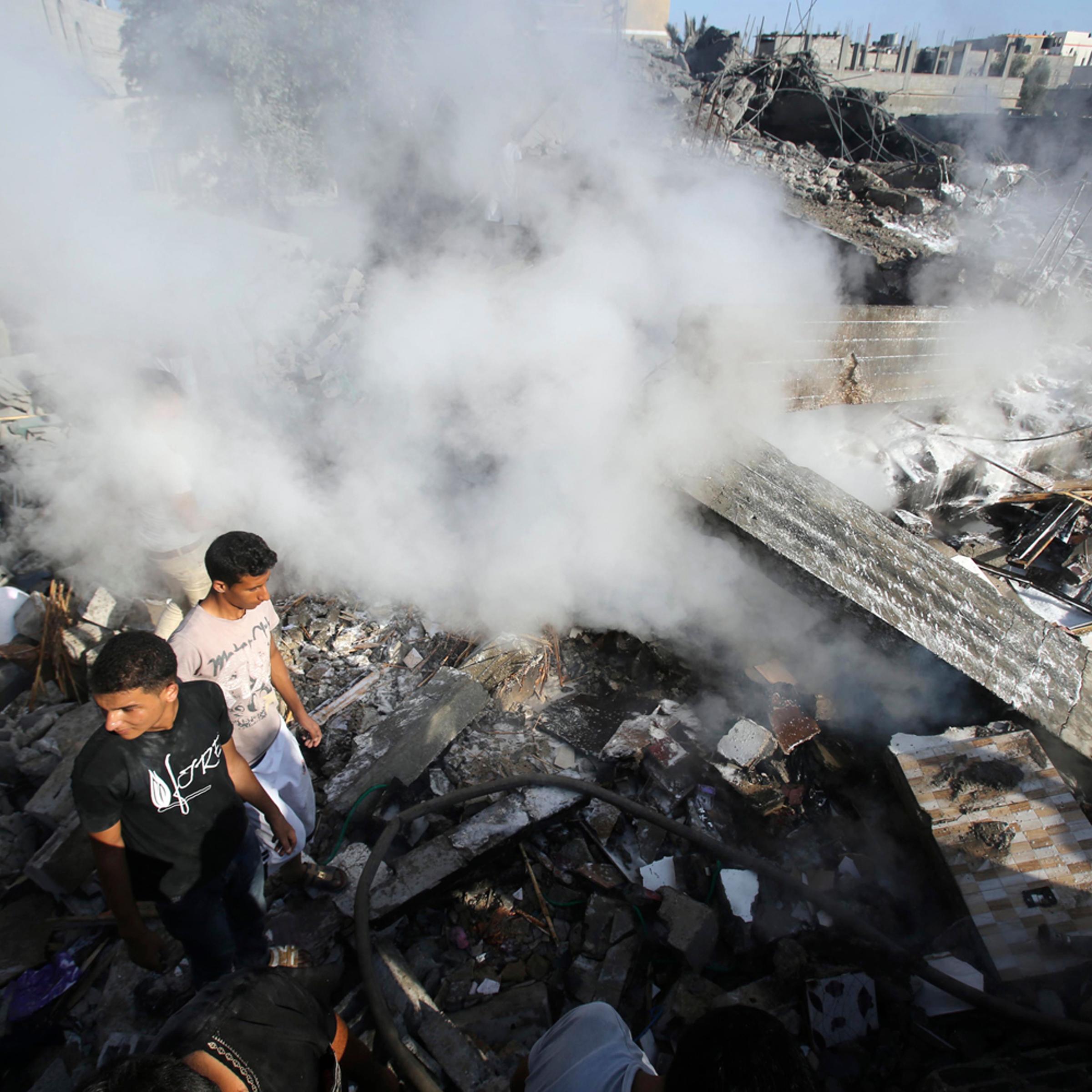 Smoke rises as Palestinians stand atop the rubble of a house, which witnesses said was destroyed in an Israeli air strike, in Rafah in the southern Gaza Strip