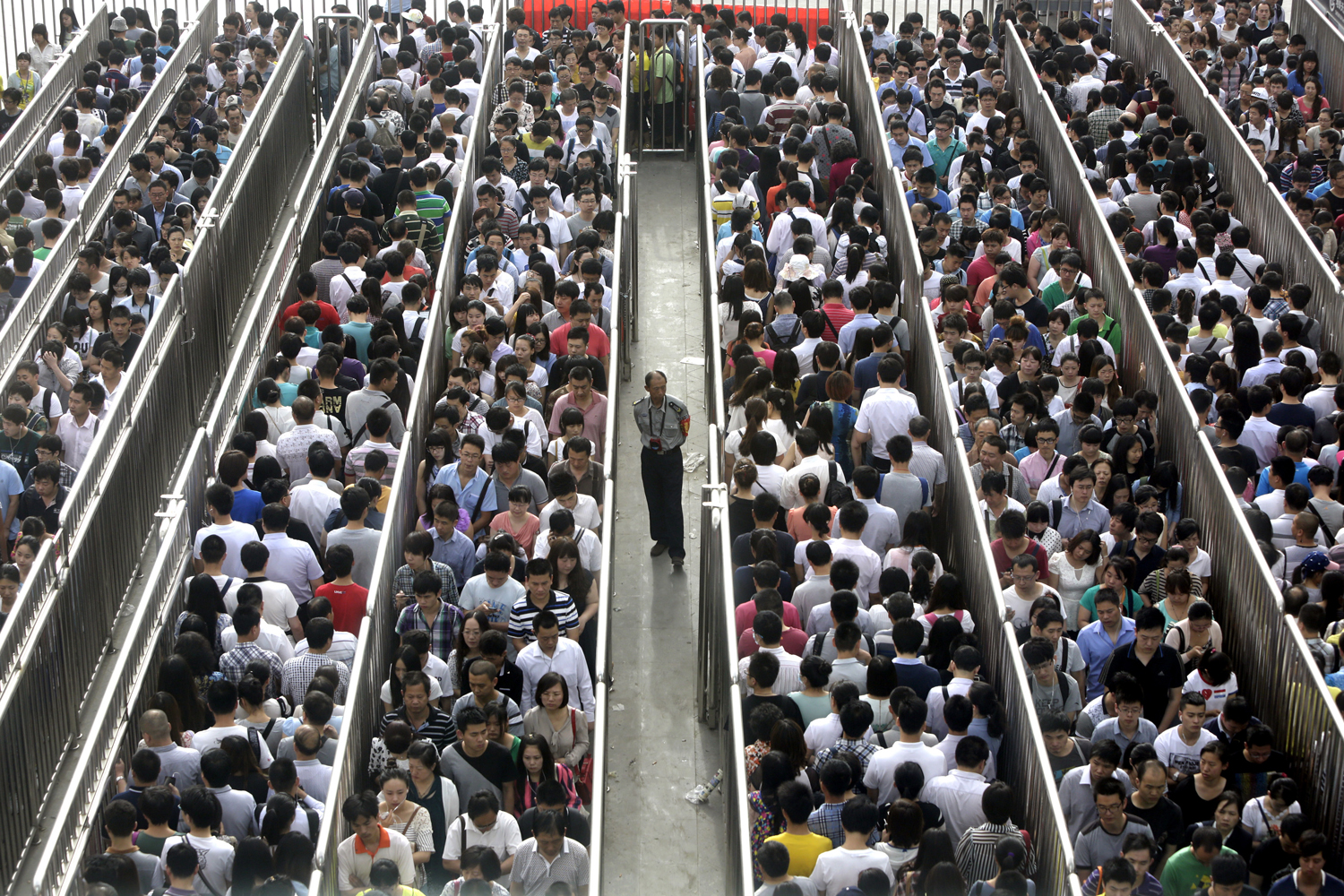 A security officer stands guard as passengers line up and wait for a security check during morning rush hour at Tiantongyuan North Station in Beijing May 27, 2014.