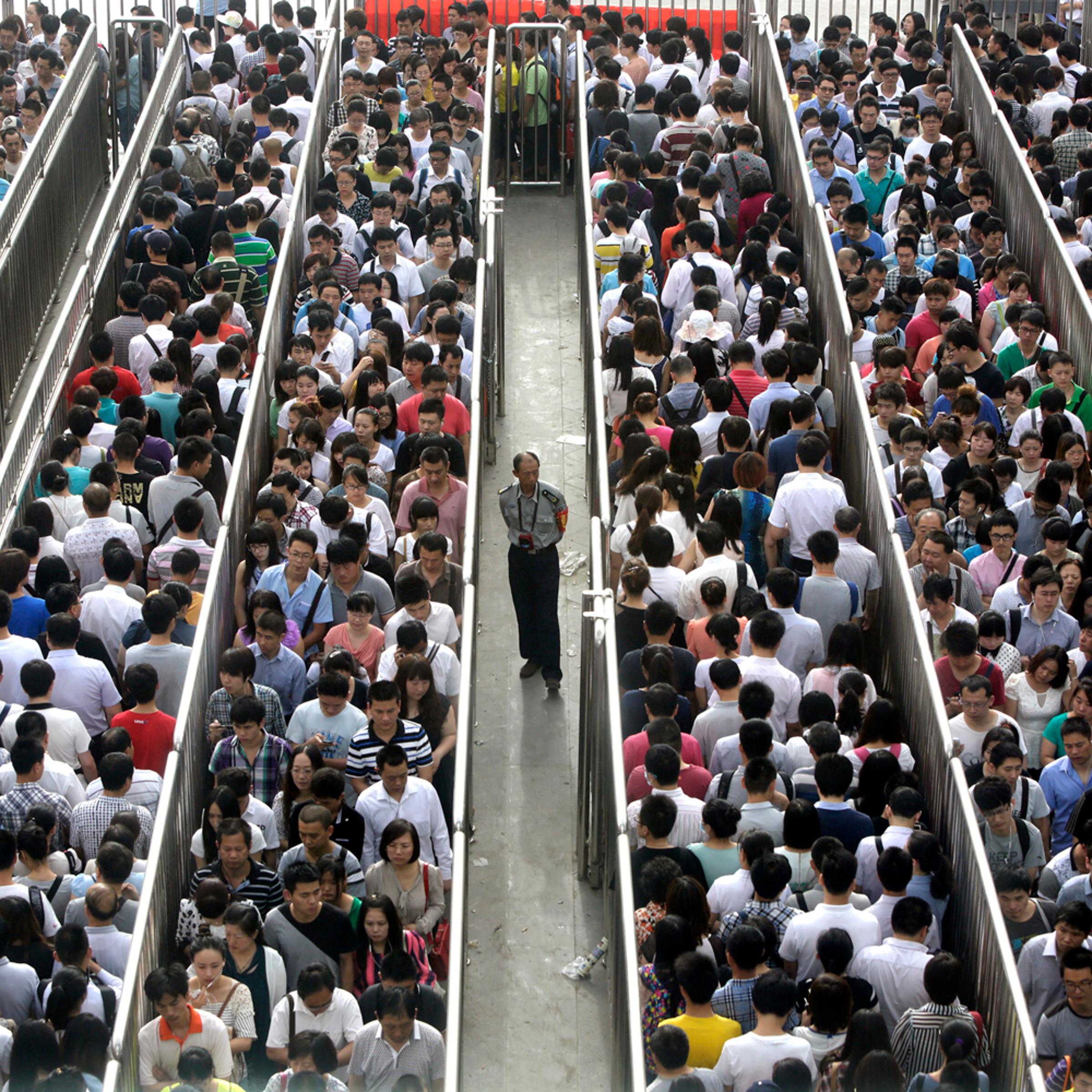 A security officer stands guard as passengers line up and wait for a security check during morning rush hour at Tiantongyuan North Station in Beijing May 27, 2014.