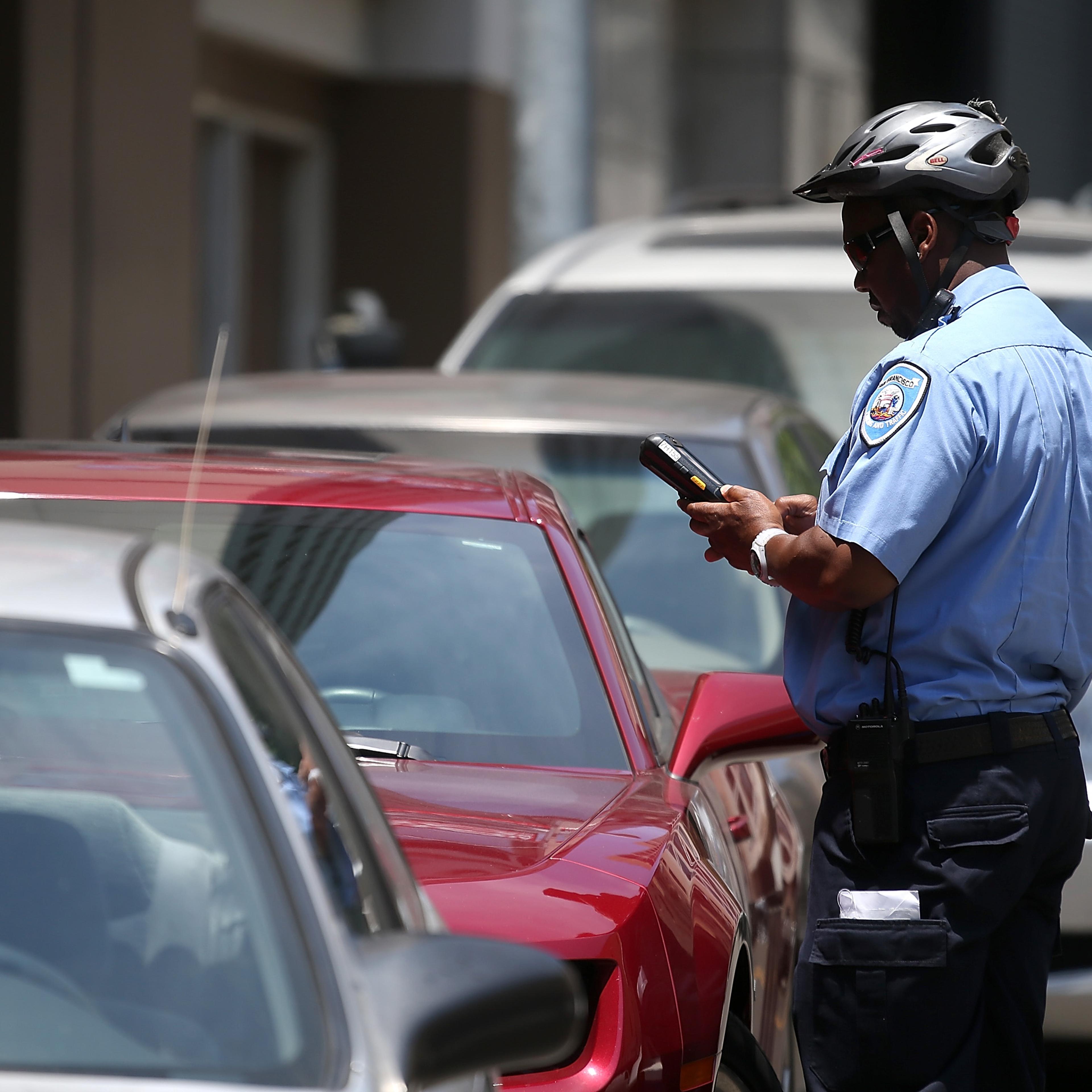 A San Francisco Municipal Transportation Agency parking control officer writes a parking ticket for an illegally parked car on July 3, 2013 in San Francisco.