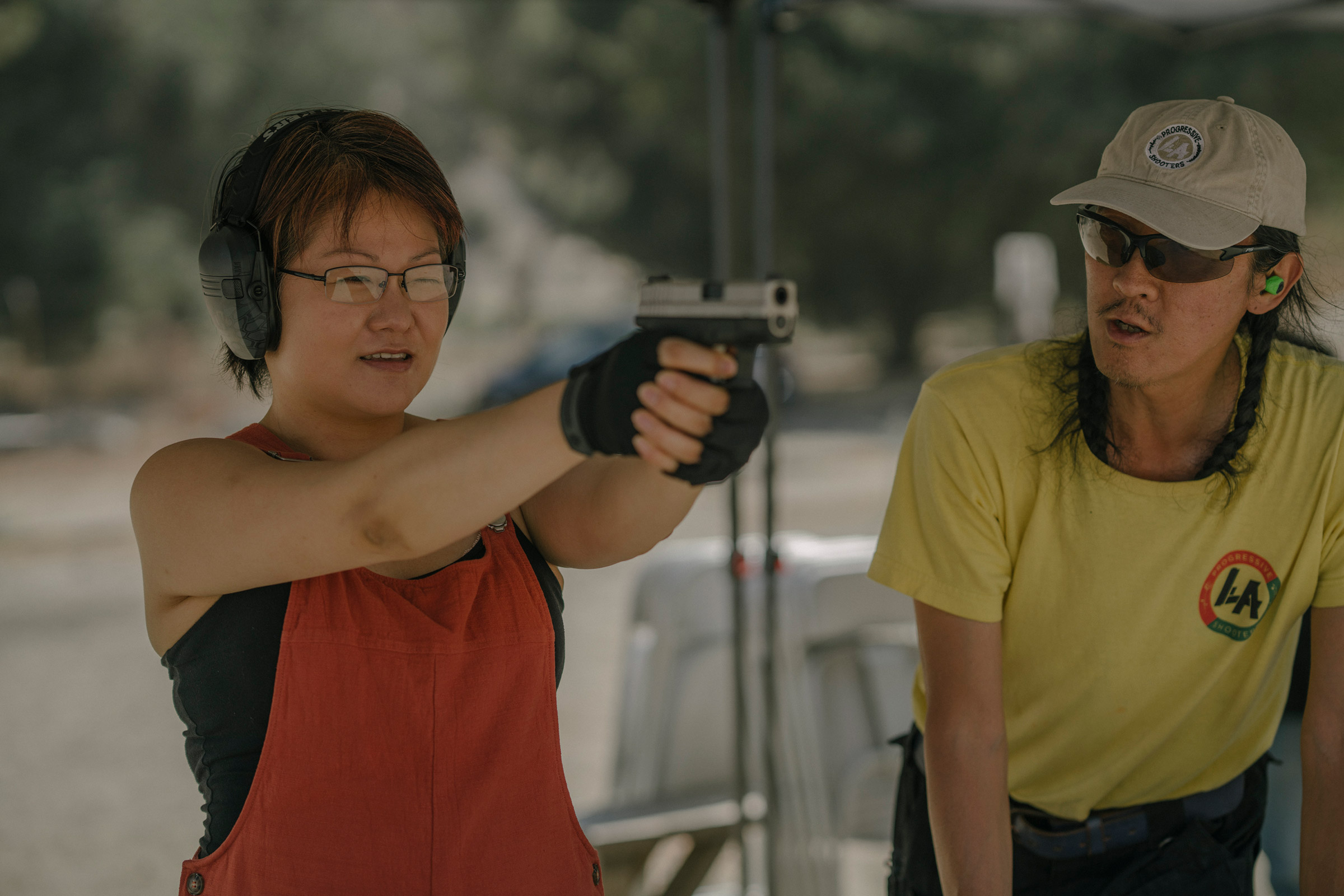 AZUSA, CALIFORNIA - JULY 18, 2021:Svetlana Kim practices shooting her handgun, while standing next to Tom Nguyen, instructor and founder of L.A. Progressive Shooters, at Burro Canyon Shooting Park in Azusa, CA. Svetlana attended beginner’s classes throug